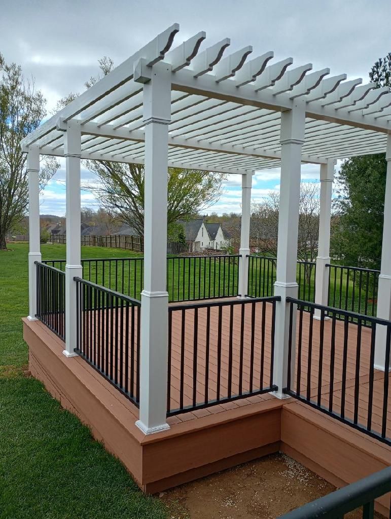 White pergola on a raised wooden deck with black railings overlooking a landscaped yard.