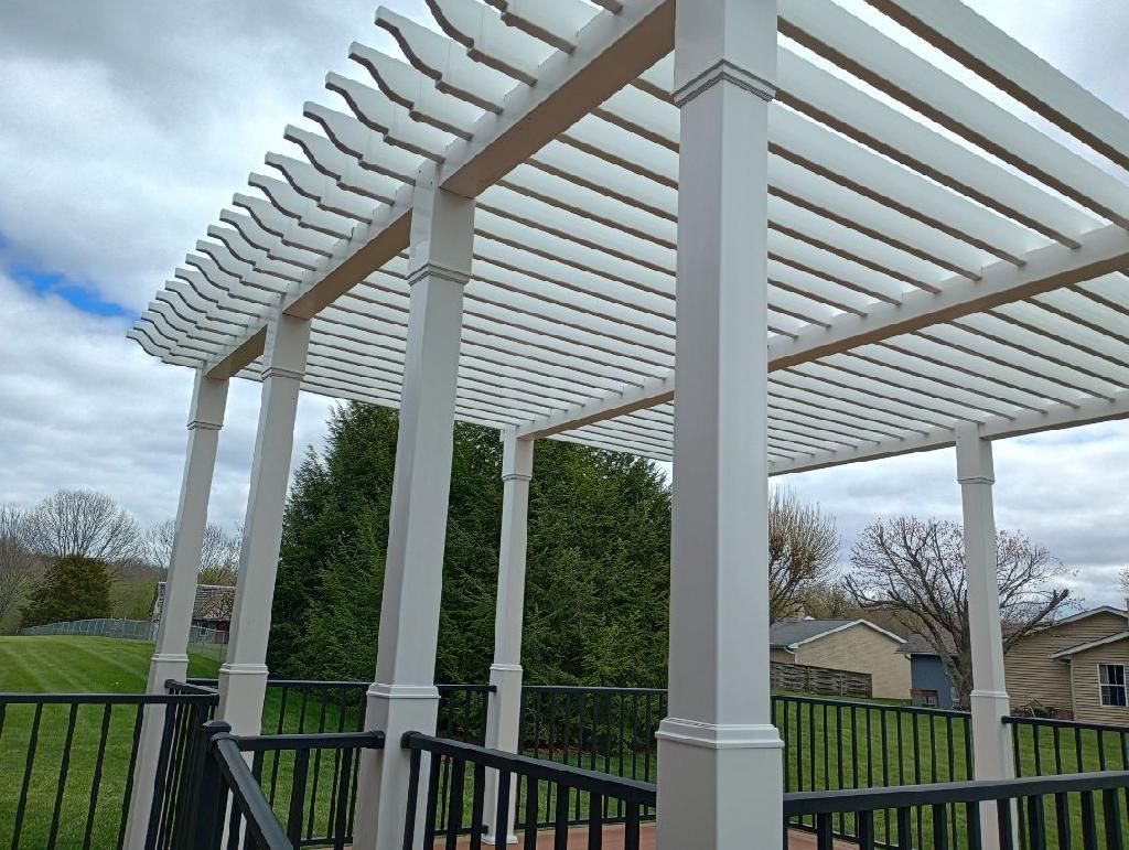 White pergola with slatted roof over a black metal railing in a grassy backyard garden