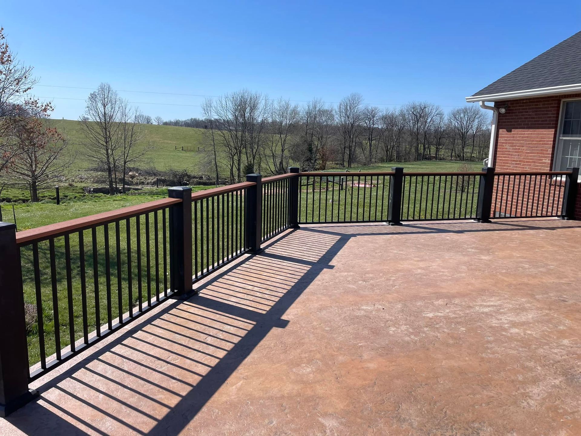 Black railing on a brick patio overlooking a sunny grassy landscape