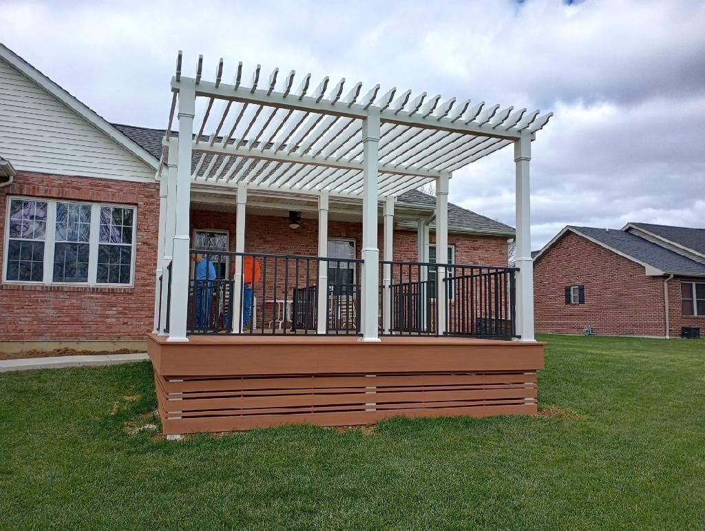 Backyard deck with white pergola, black railing, and brick house in the background