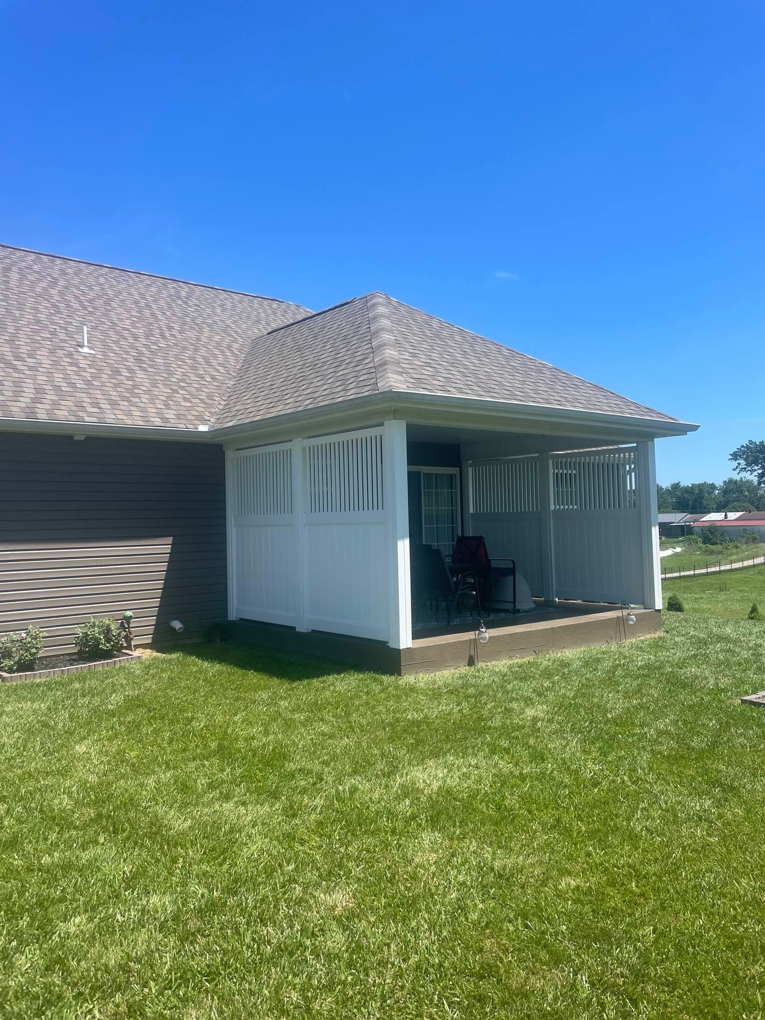 White house corner with porch, gray shingle roof, and green lawn under a bright blue sky