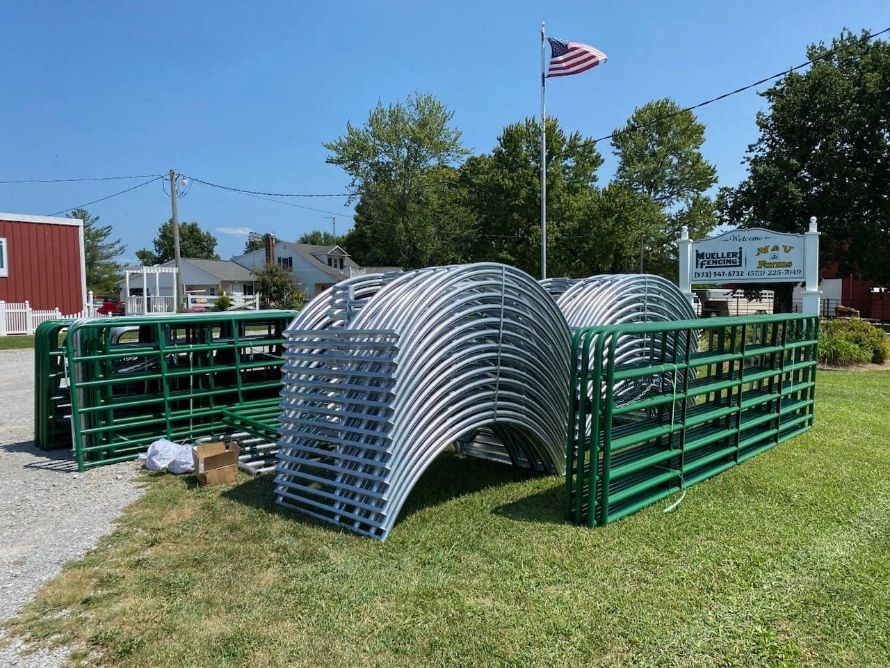 Stacks of green and silver metal barricades on grass under a blue sky, with an American flag in the background
