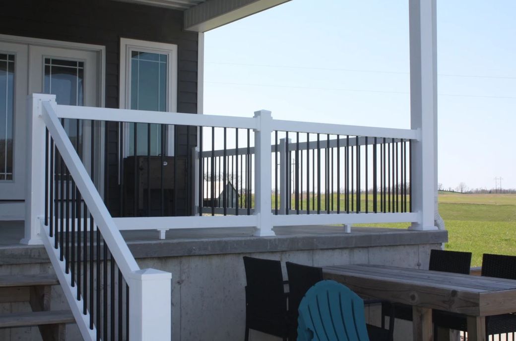 White-railed deck with black balusters beside a house, overlooking an open field