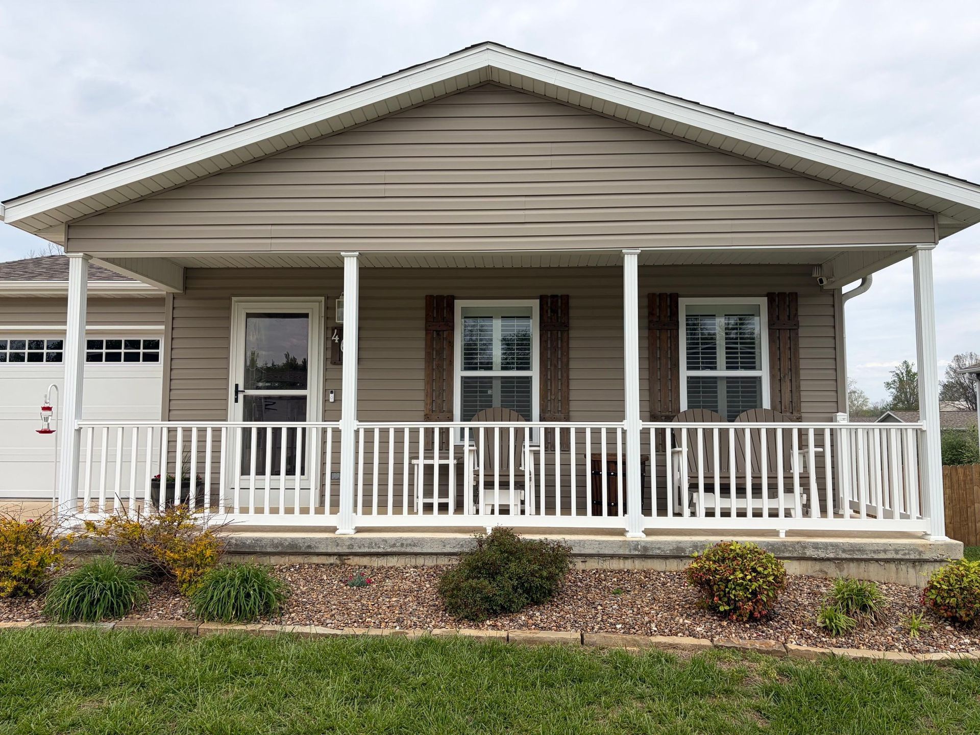 Single-story beige house with a white porch railing and columns, centered front view.