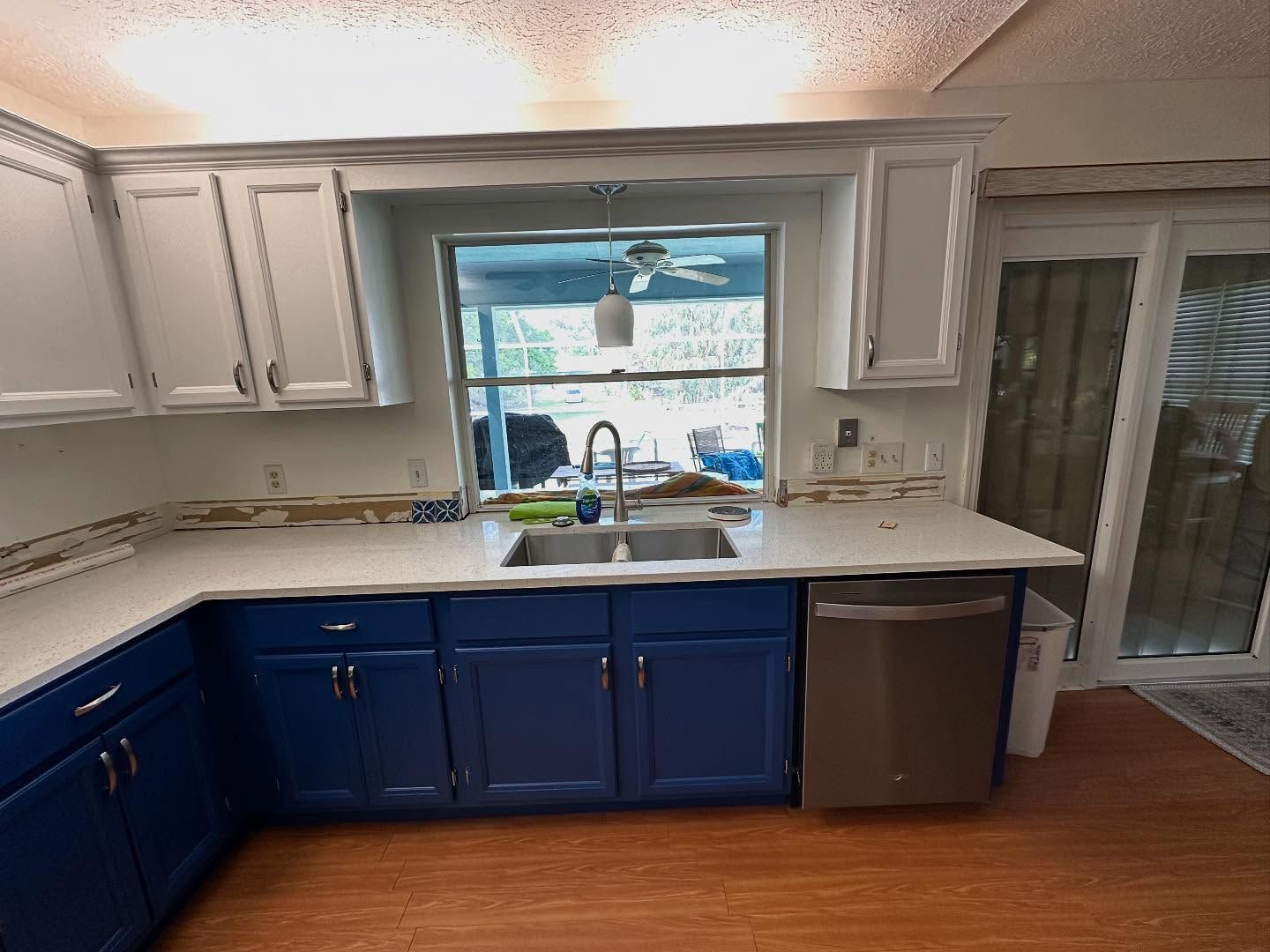 Bright kitchen with blue lower cabinets, white counters, and a window over the sink.