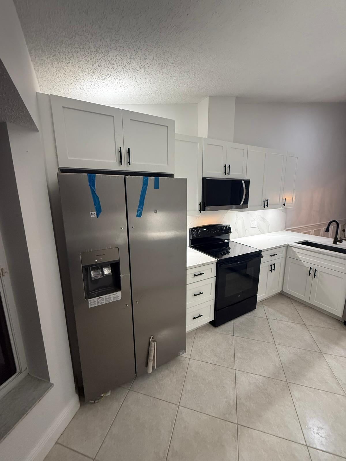 Modern white kitchen with stainless steel refrigerator, black stove, white cabinets, and tiled floor