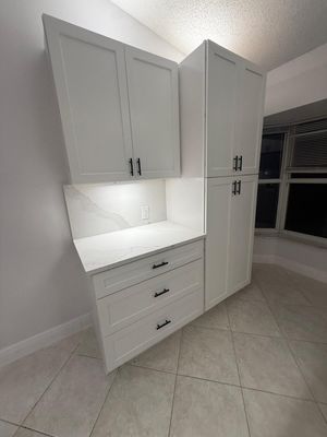 White built-in cabinets and drawers in a bright tiled room with a corner countertop and window.