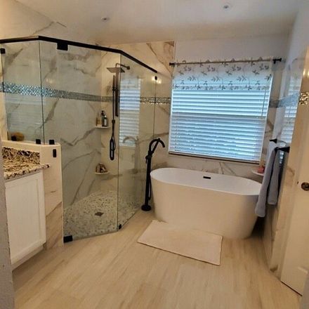 Modern bathroom with glass shower, freestanding tub, window blinds, and light wood flooring