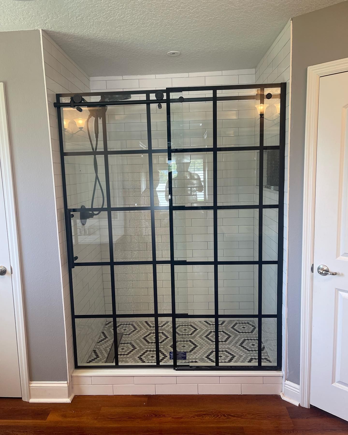 Glass shower enclosure with black grid framing in a bathroom alcove, with patterned tile floor.