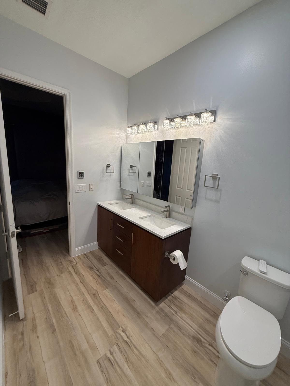 Modern bathroom with gray walls, wood vanity, mirror, sink, toilet, and open doorway to a dark room