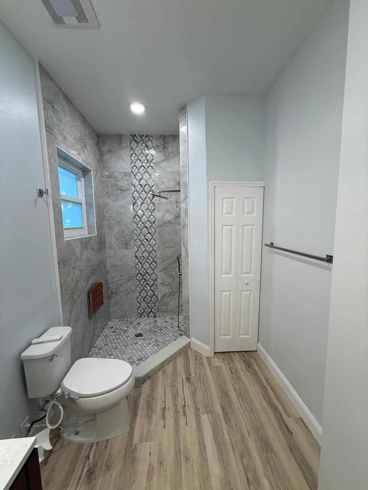 Modern bathroom with tiled shower, toilet, vanity area, and wood-look floor.