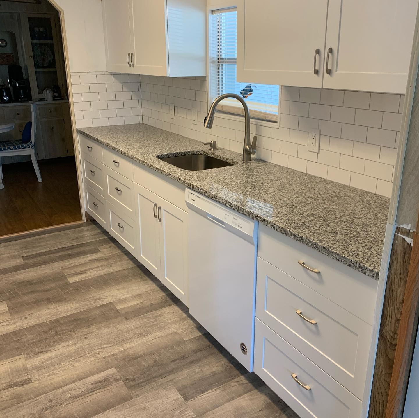 Bright white kitchen with granite countertops, subway tile backsplash, and a stainless sink under a window.