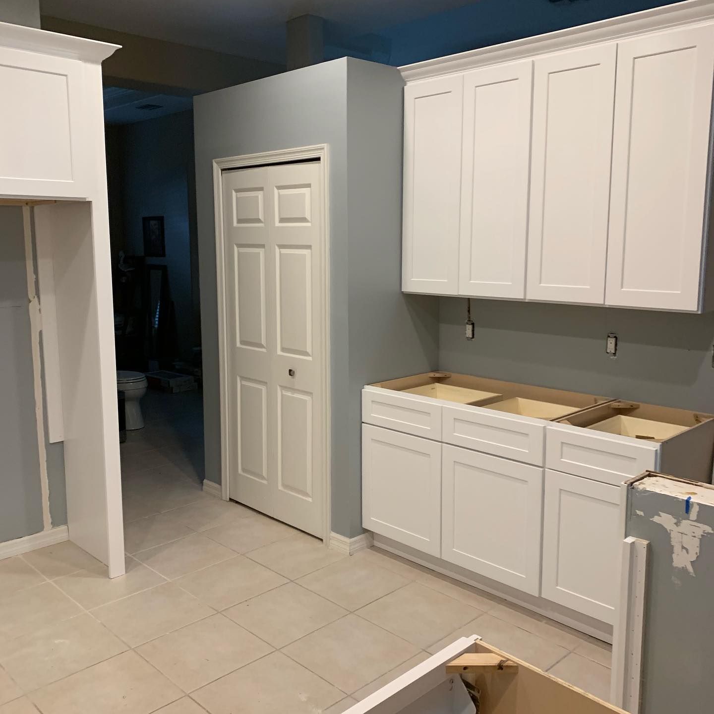 White kitchen with tile floor, upper and lower cabinets, countertop, and a closed pantry door.