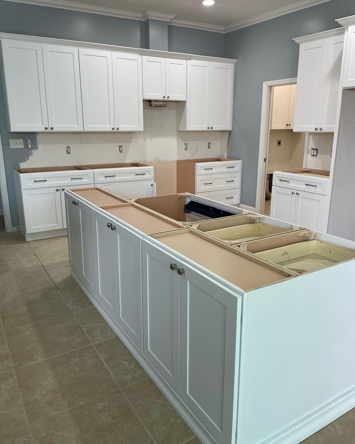 Bright white kitchen with unfinished island cabinets and tiled floor, viewed from the center of the room
