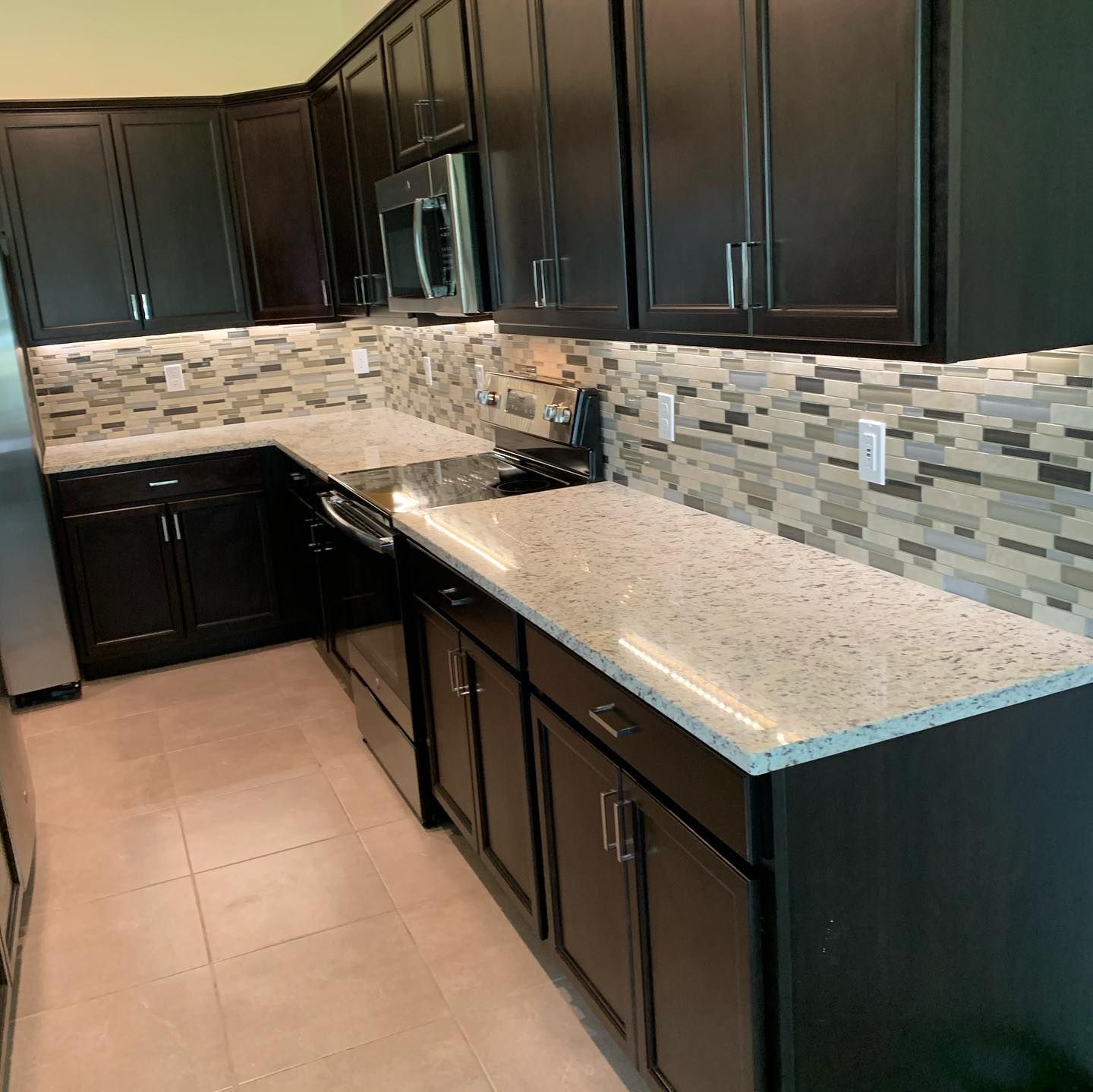 Modern kitchen with dark cabinets, speckled countertops, tile backsplash, and stainless steel appliances
