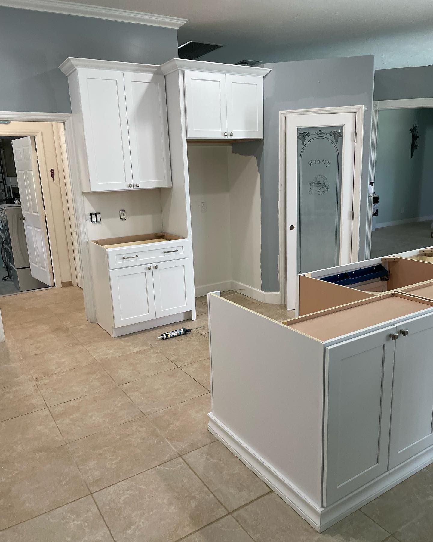 Partially renovated kitchen with white cabinets, beige tile floor, and a kitchen island under construction