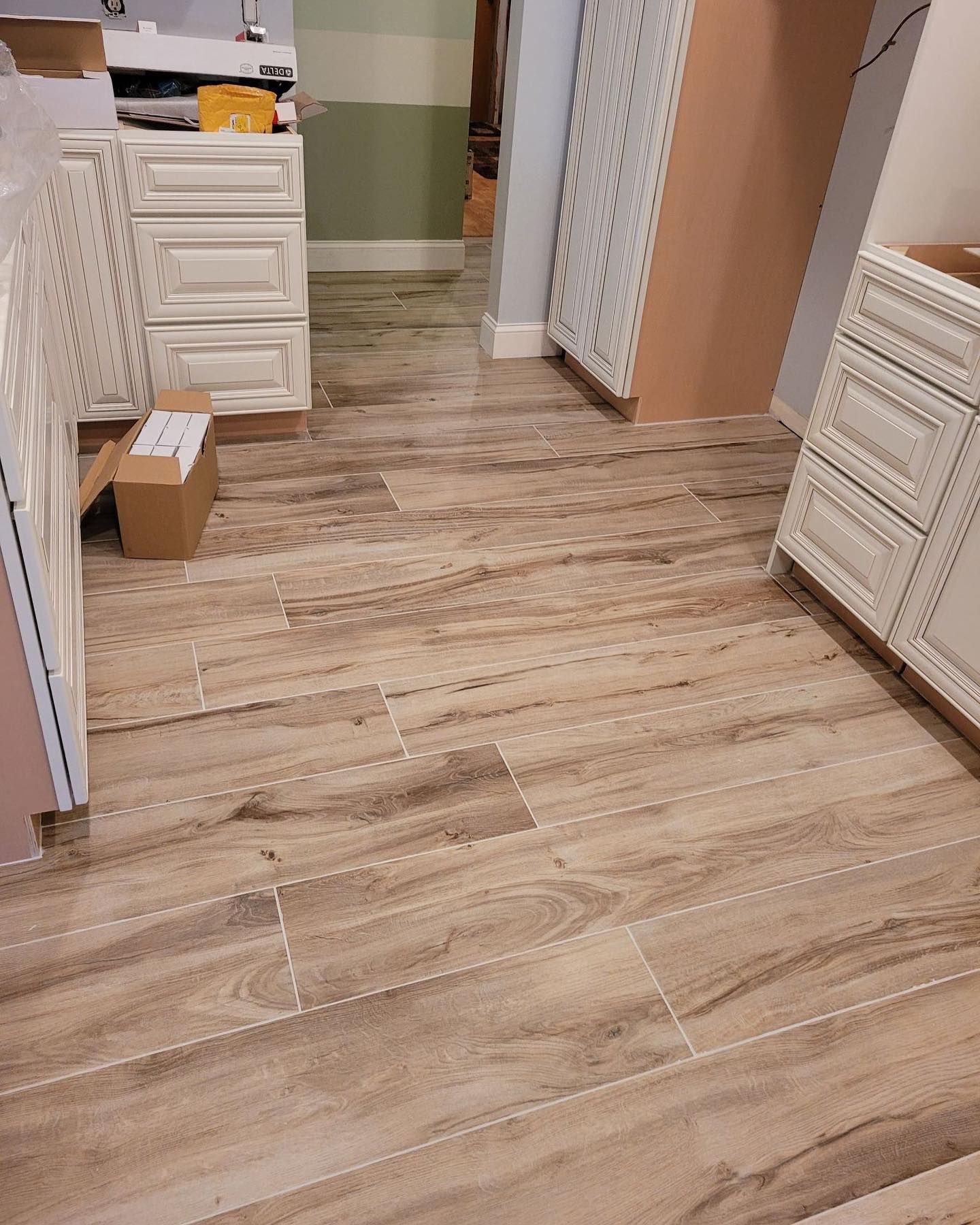 Wood-look tile floor in a bathroom or closet area with white vanities and a cardboard box