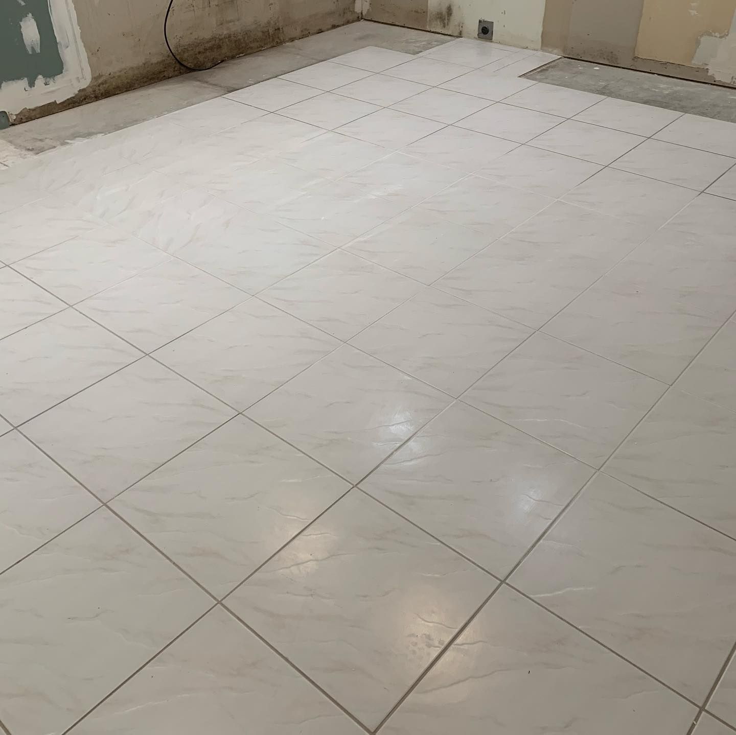 Empty tiled room with beige walls and a glossy white floor.