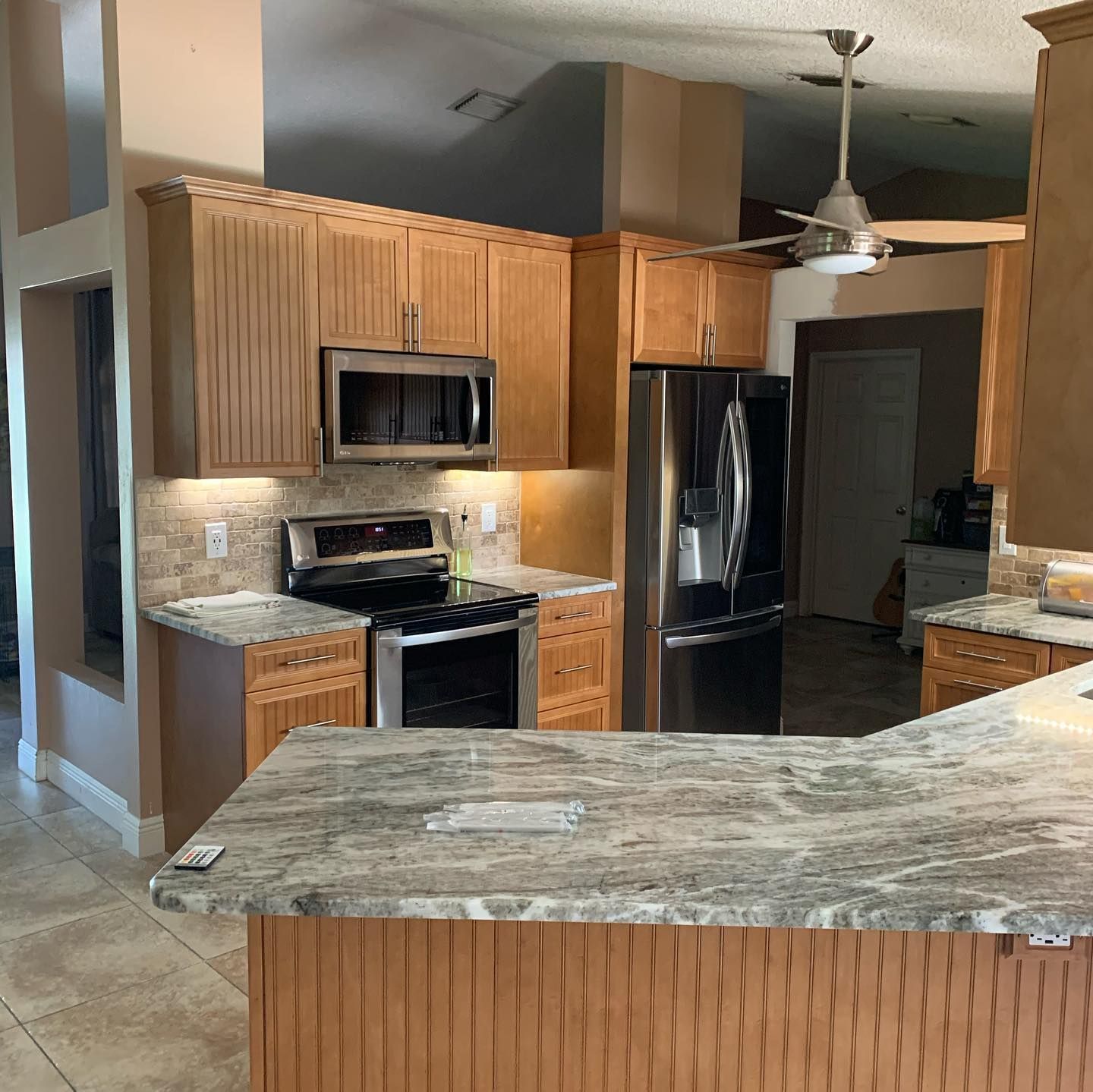 Modern kitchen with wooden cabinets, stainless steel appliances, granite counters, and a ceiling fan