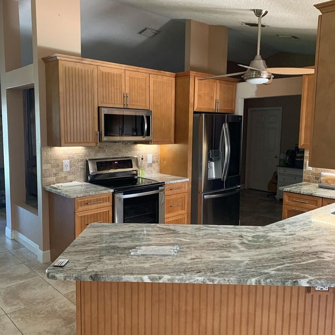 Modern kitchen with wooden cabinets, stainless steel appliances, granite counters, and a ceiling fan