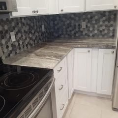 Modern kitchen corner with black stove, white cabinets, gray mosaic backsplash, and marble-look countertops