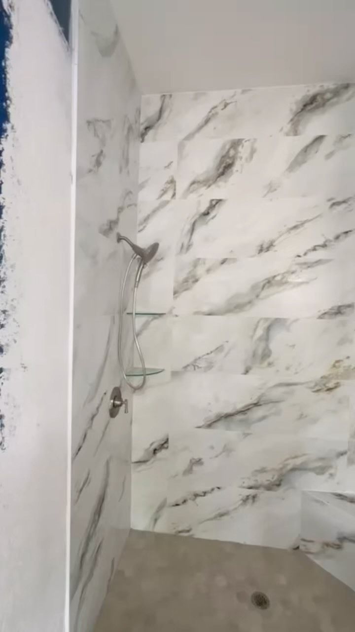 Empty tiled shower corner with marble-pattern walls and plumbing fixture visible.