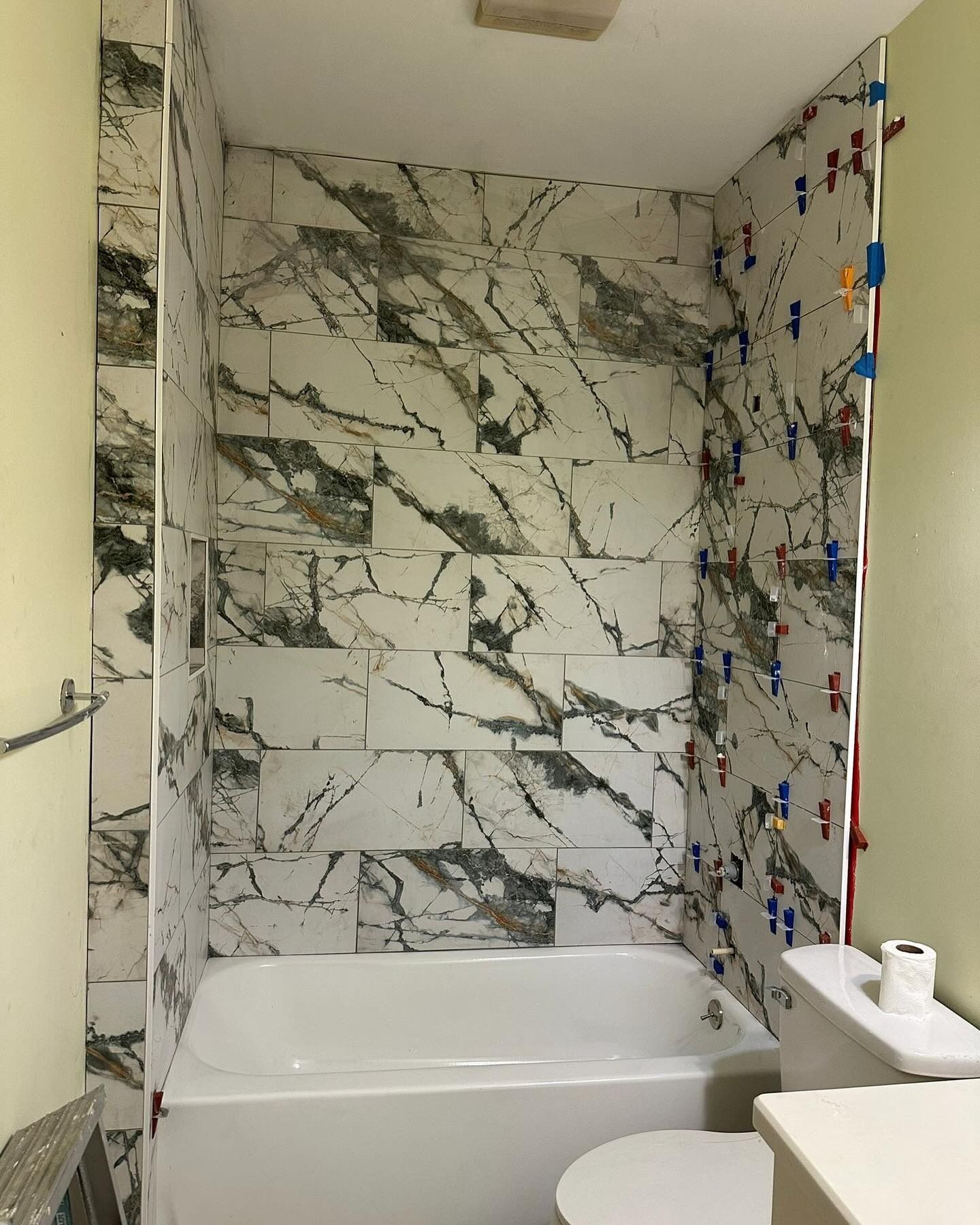 Small bathroom with a marble-tiled alcove bathtub and blue accent wall tiles.