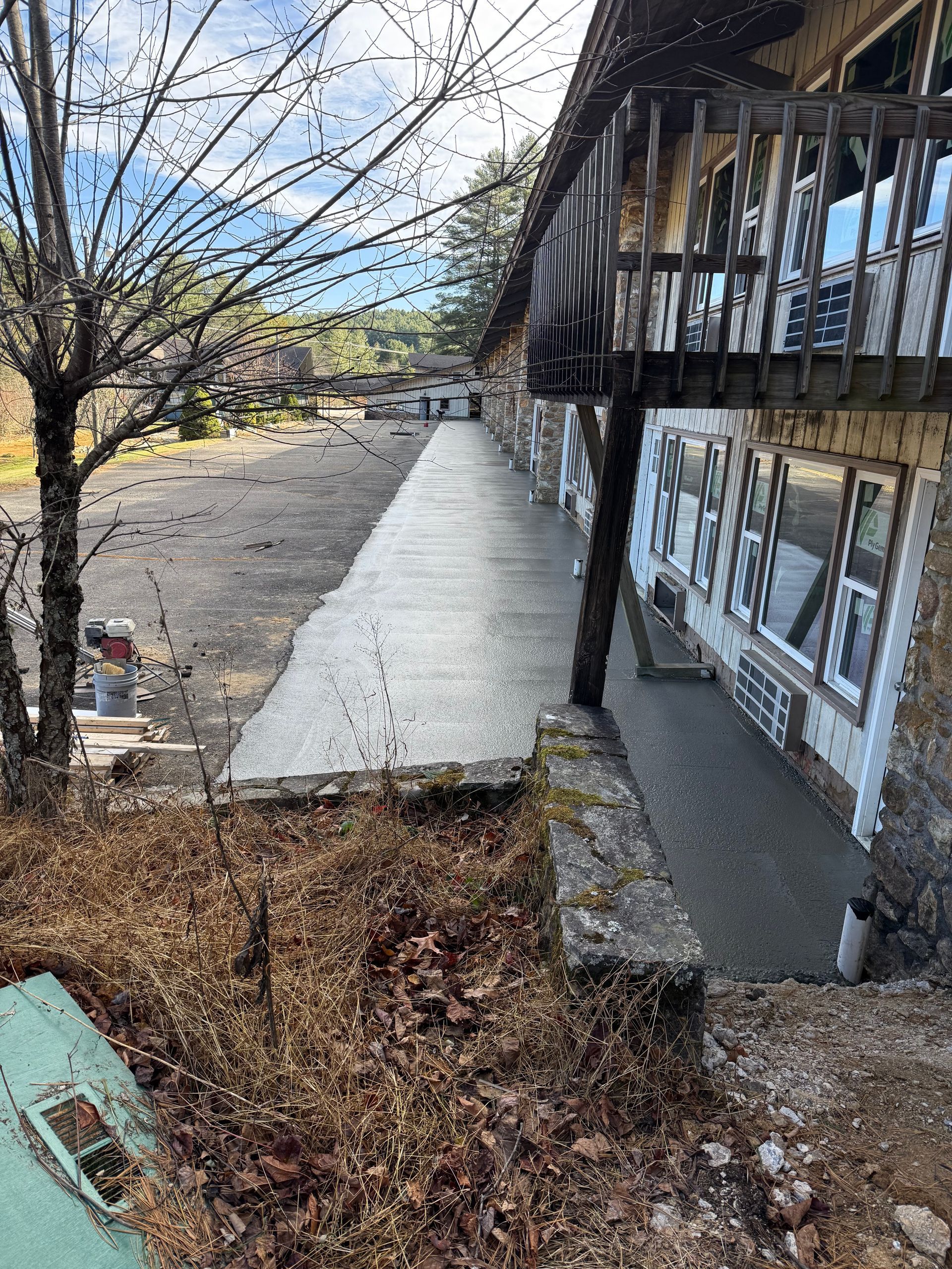 A multi-story hotel with a wooden balcony overlooking a recently poured concrete walkway and a large, gravel parking lot.