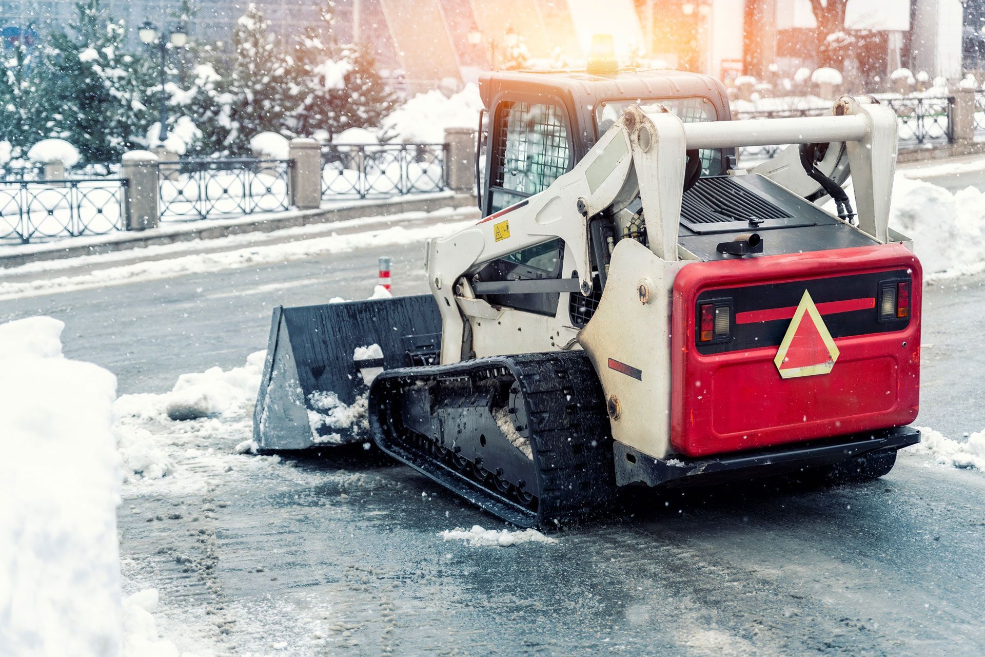 Snowplow clears snow from a city street, white and red machine with tracks, winter setting.