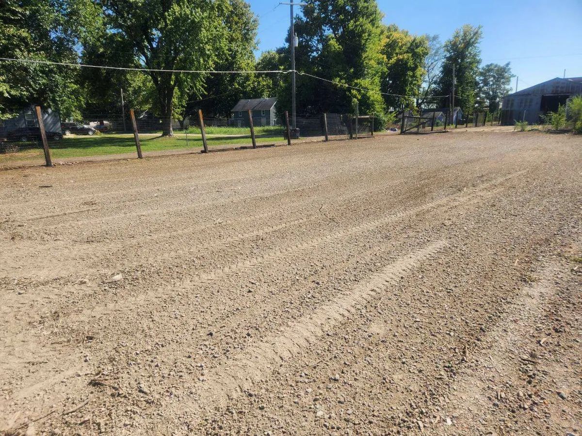 A dirt road with a fence and trees in the background