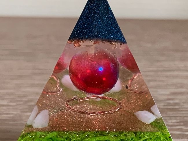 Orgonite. Een piramide met een rode bal in het midden op een tafel.