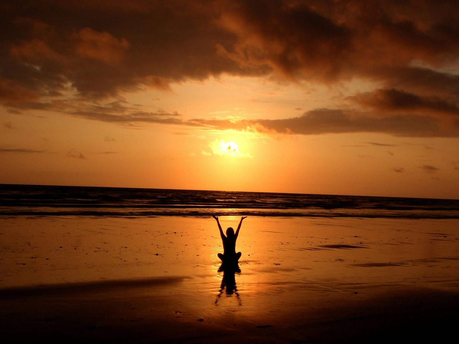 Een persoon staat op een strand bij zonsondergang met zijn armen in de lucht