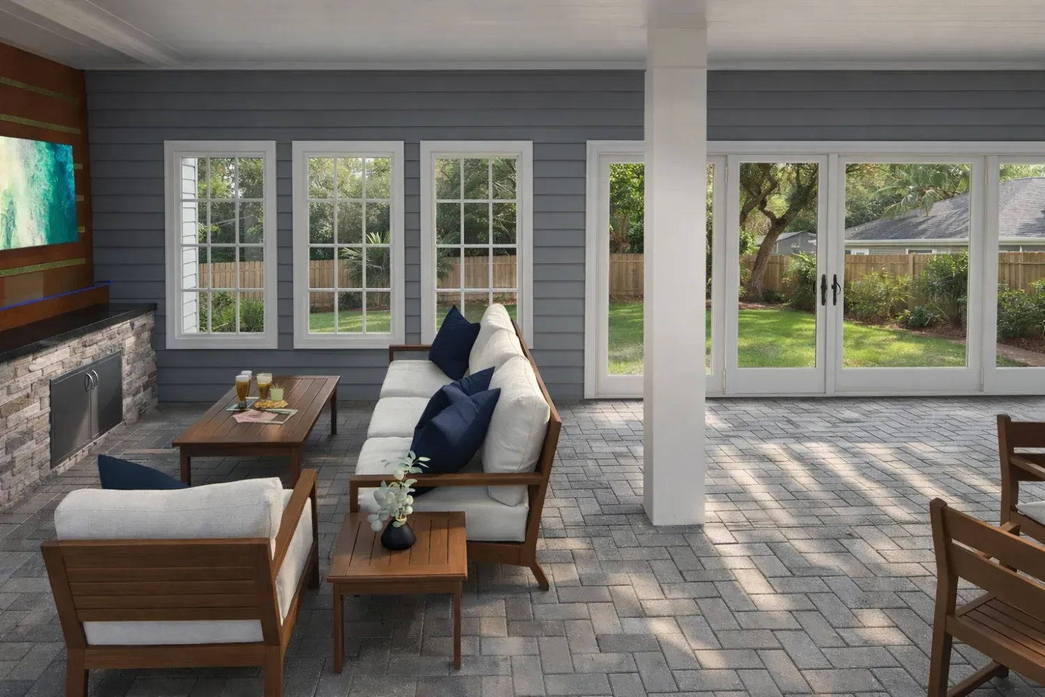 A modern covered patio with stone flooring, outdoor lounge furniture, a fireplace, and large glass doors leading outdoors.