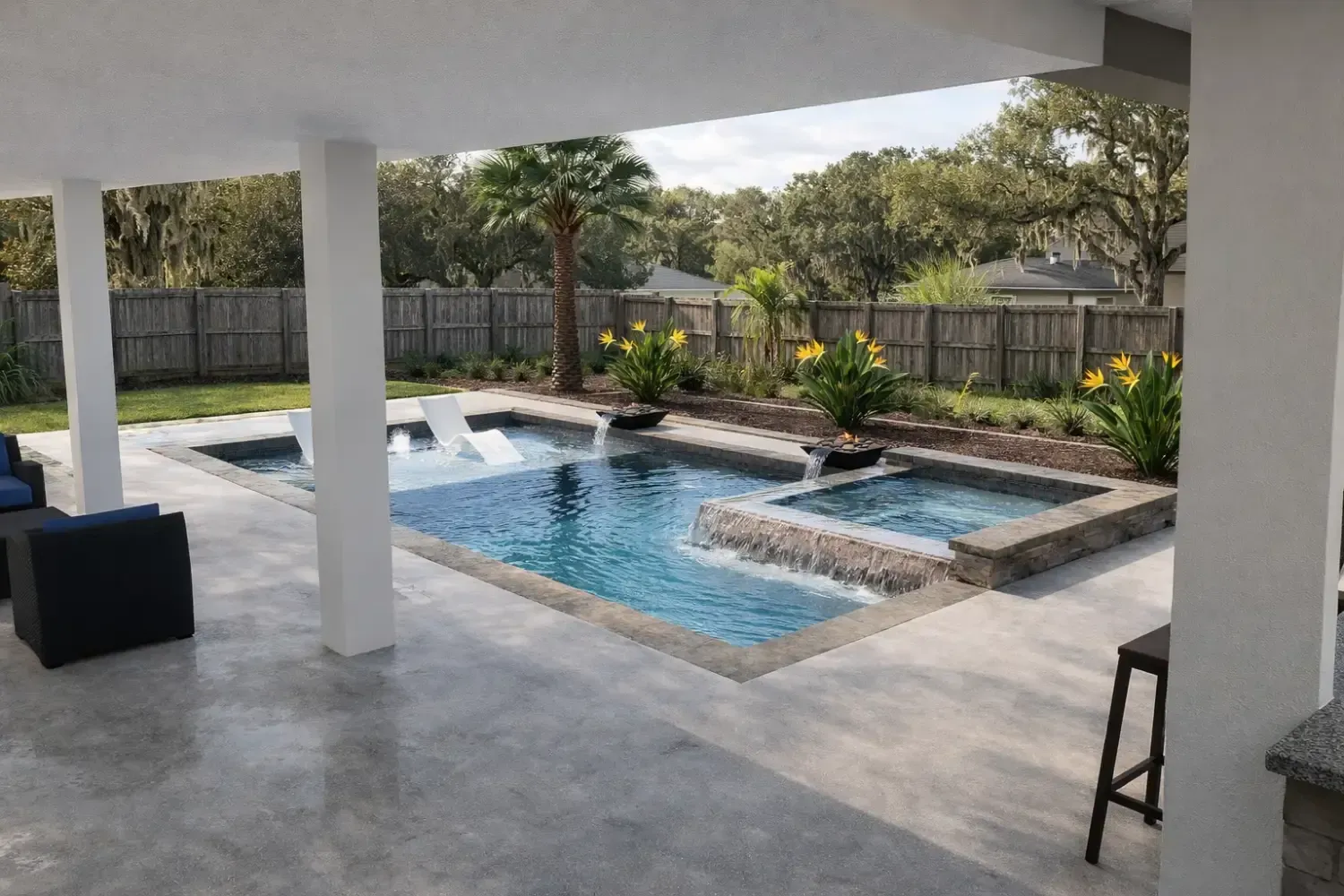 A view from a covered patio overlooking a modern rectangular swimming pool with an integrated hot tub and sun shelf.