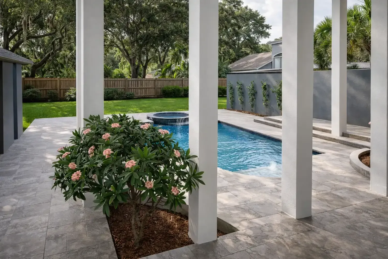 A view from a patio with white columns overlooking a blue swimming pool and a green backyard lawn.