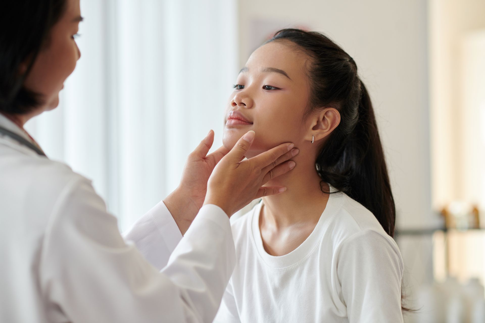 A doctor gently examining a young girl's neck during a routine medical checkup.