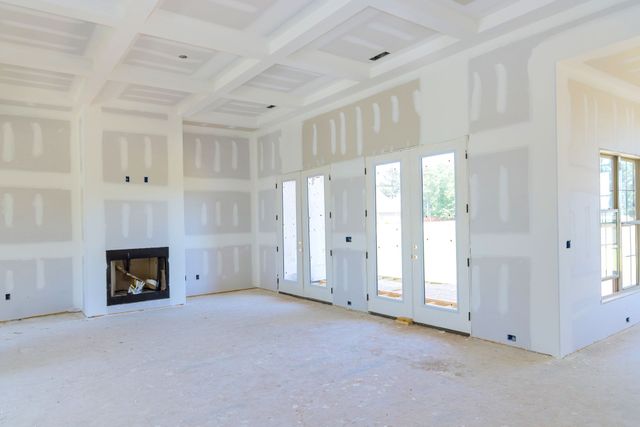 Empty unfinished living room with white drywall, fireplace, and large glass doors opening outside