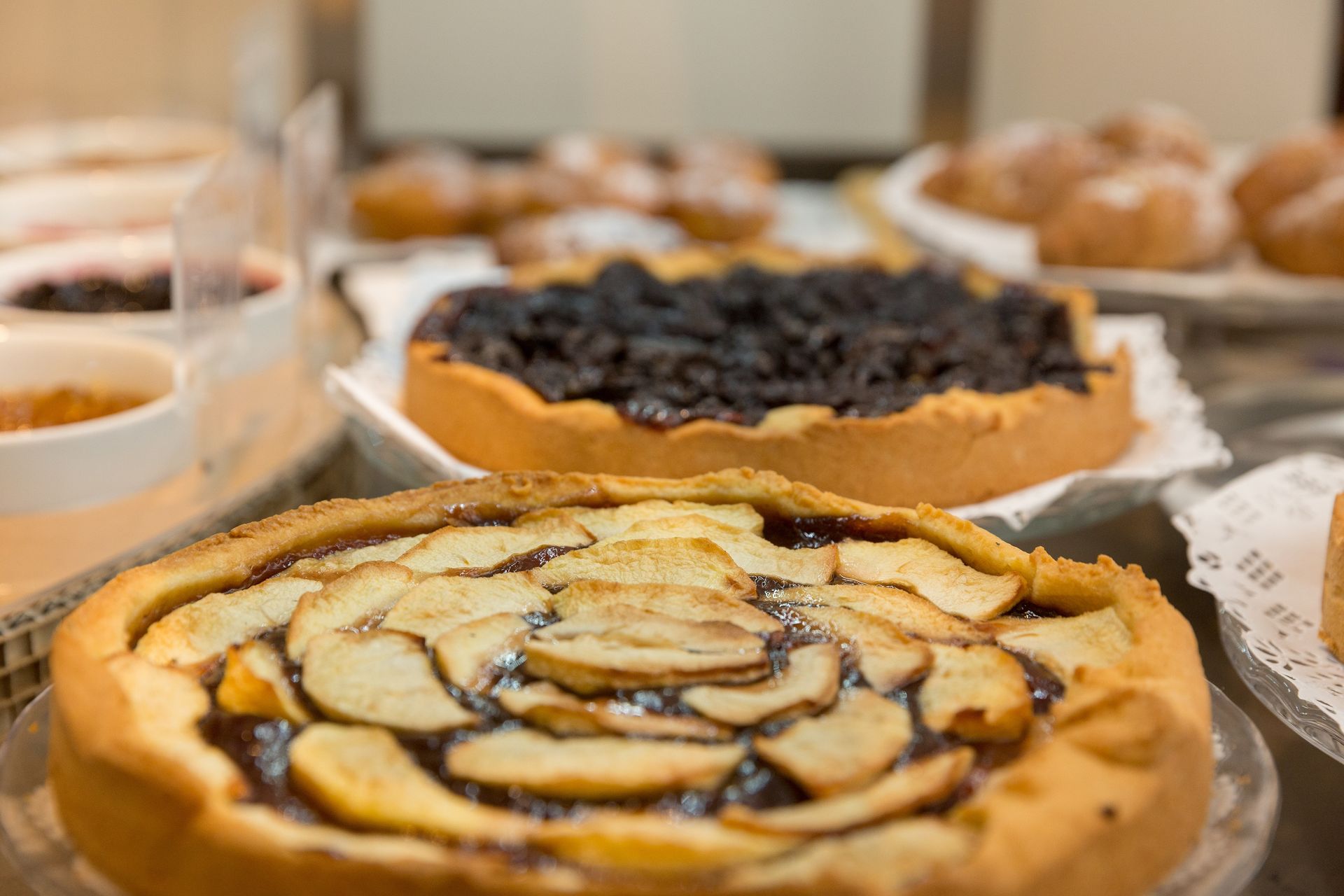 Pastries on a buffet table, including a fruit tart in front and a berry tart behind it