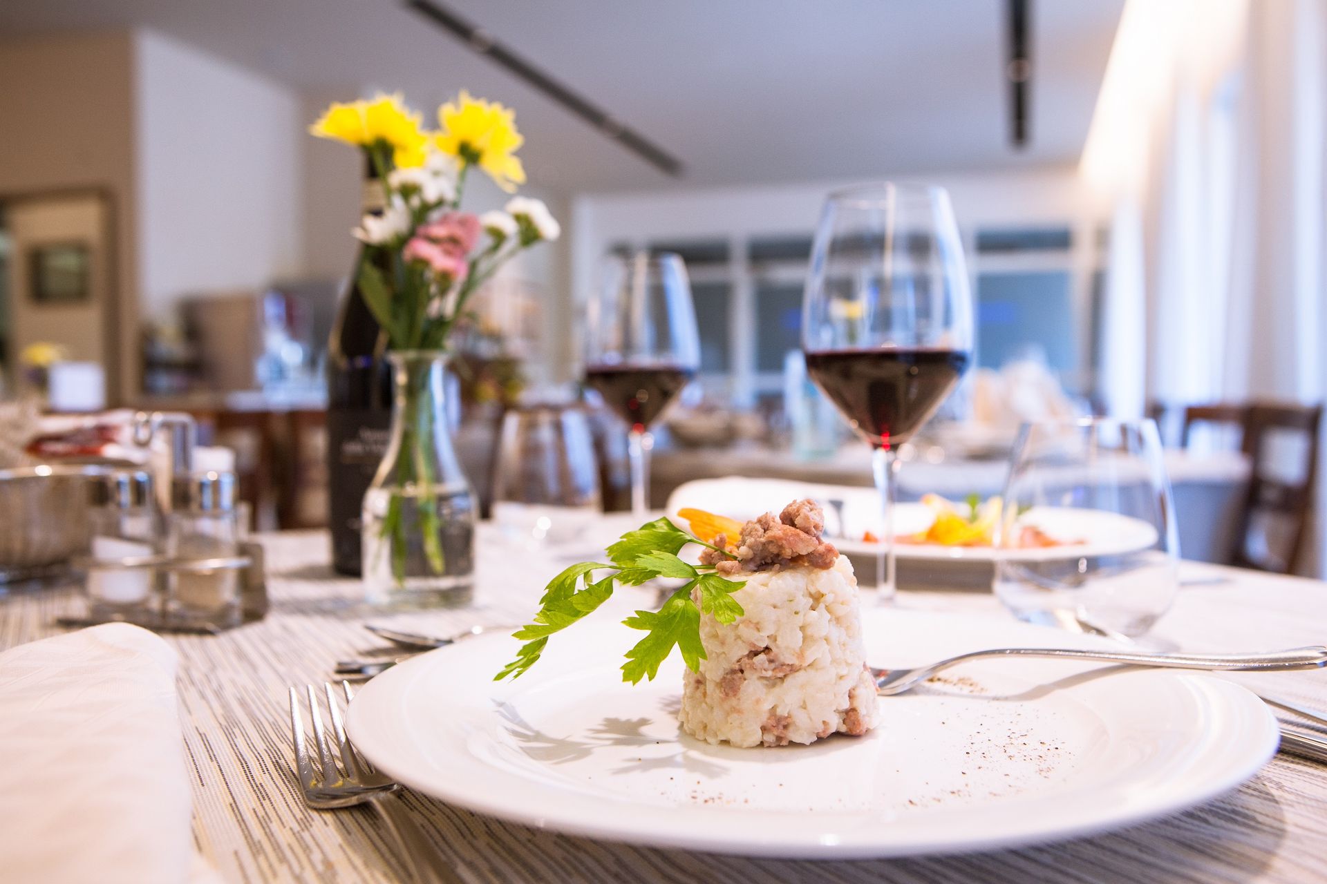 Elegant plated appetizer on a restaurant table with wine glass and flowers in the background