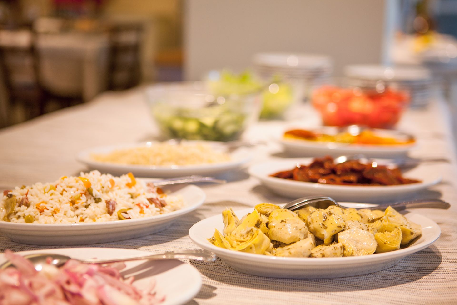 Buffet table with several plated dishes, including pasta, salad, and meat, in a warm indoor setting