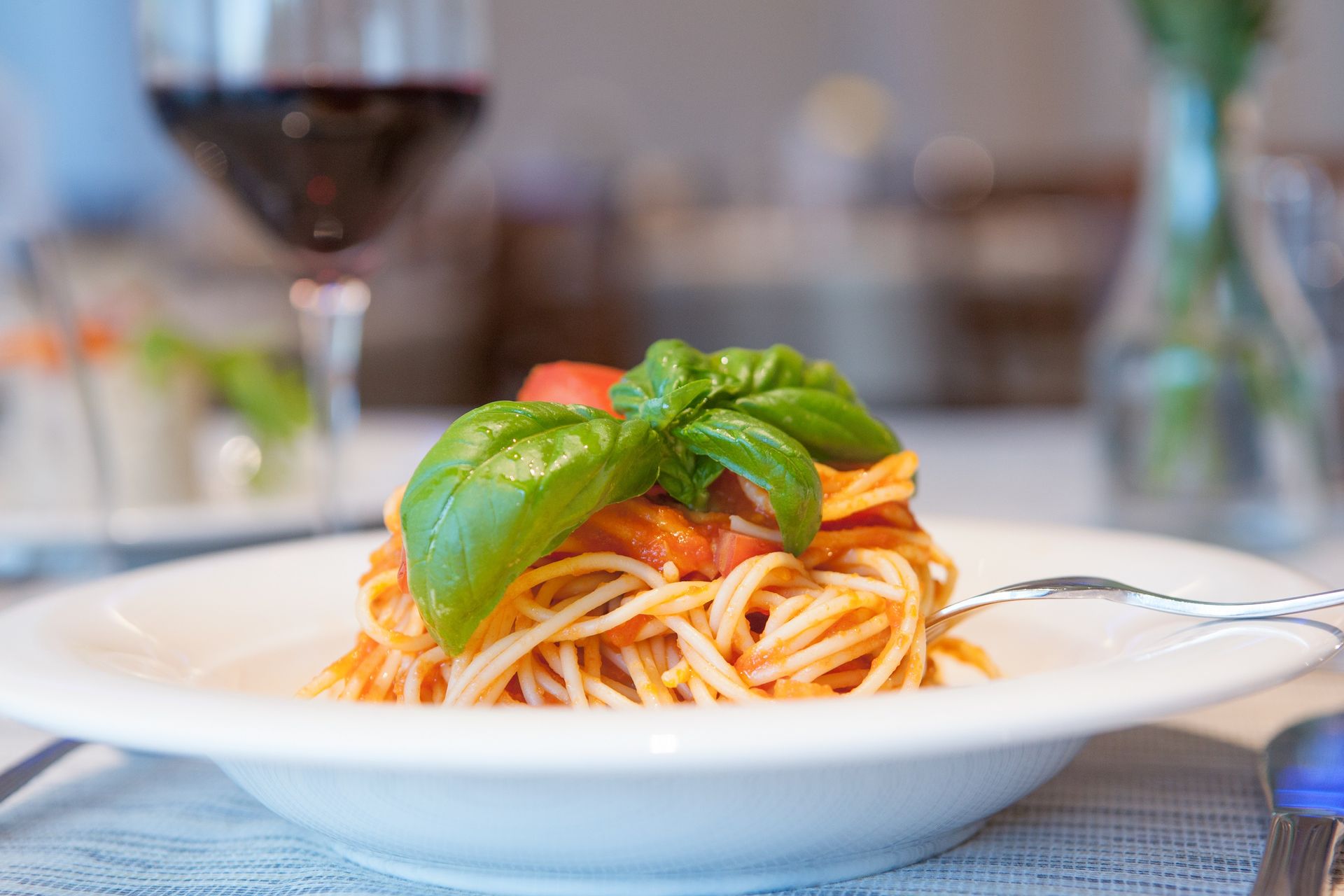 Plate of spaghetti with tomato sauce and basil on a table with a wine glass in the background
