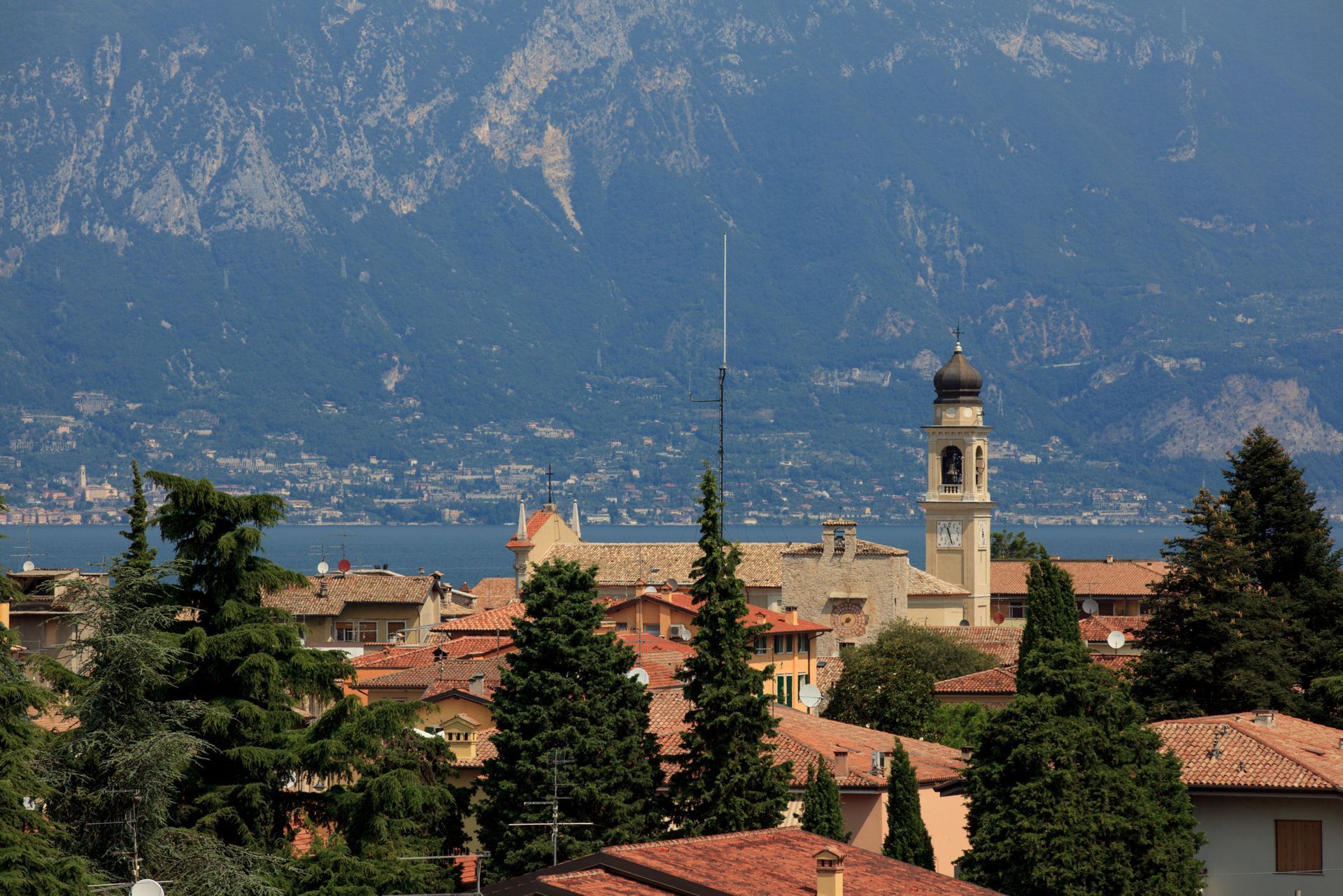 Town rooftops and church tower beneath mountains on a clear day