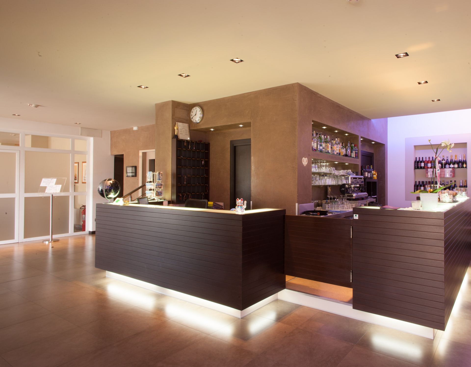 Reception moderna dell'hotel con banconi in legno scuro, illuminazione calda e pavimento della hall lucido.