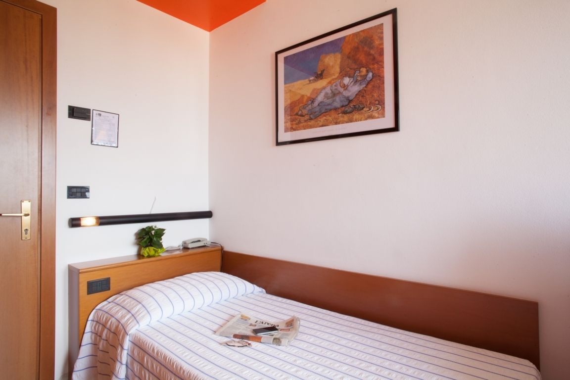 Small bedroom with a single bed, white walls, orange ceiling, and framed artwork above the headboard