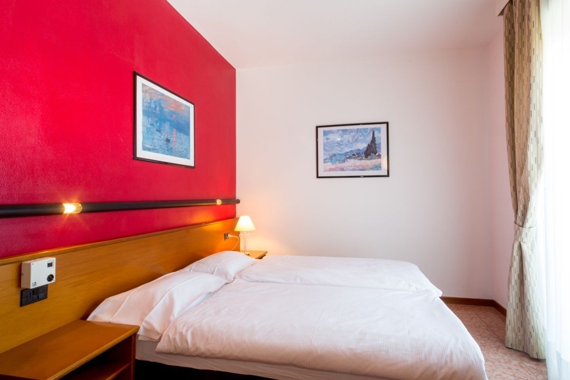 Modern bedroom with red accent wall, white bed, bedside lamp, and framed artwork