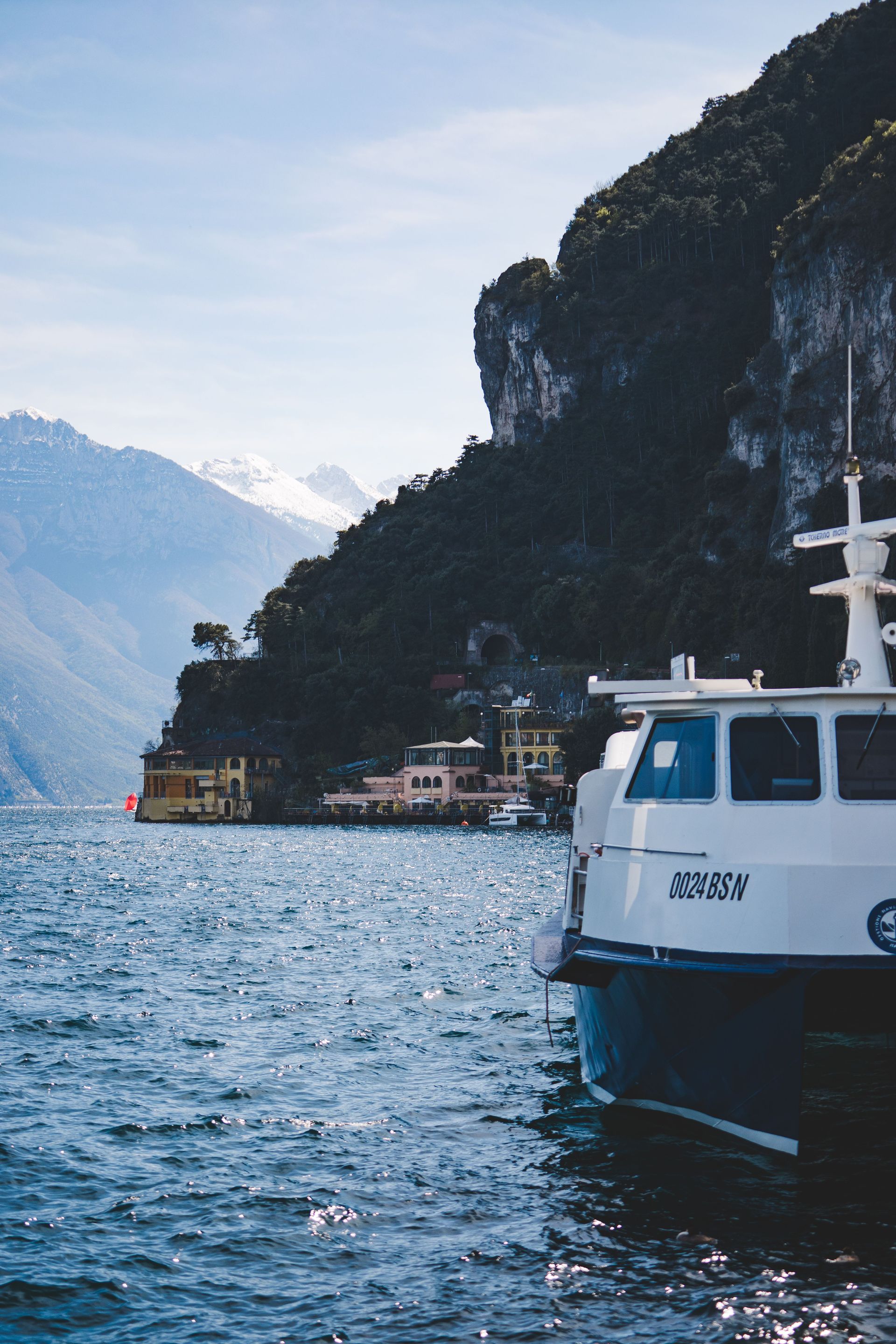 Boat on a choppy blue lake beside steep rocky cliffs and distant mountains.