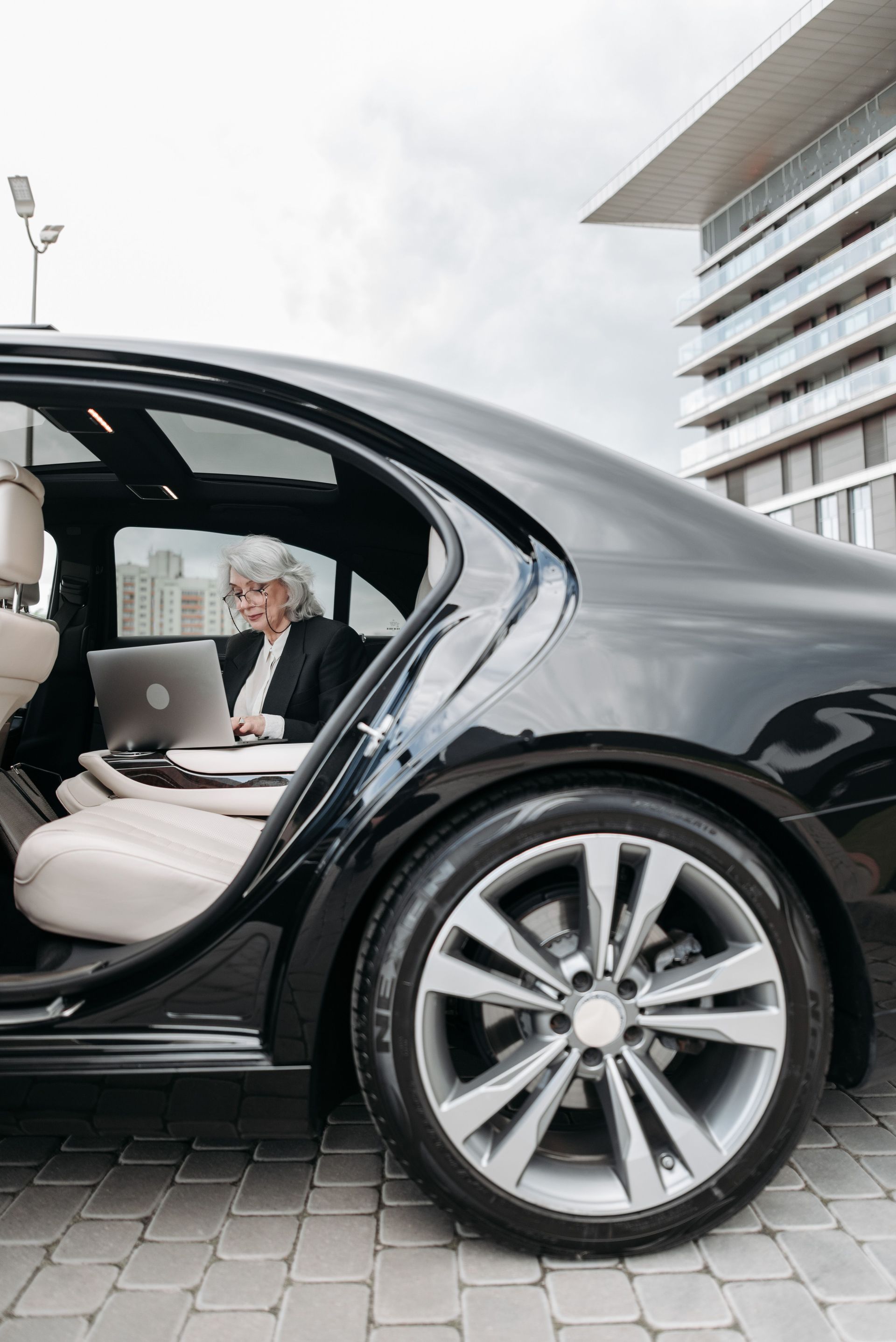 Luxury black car with open rear door and white interior parked outside a modern building