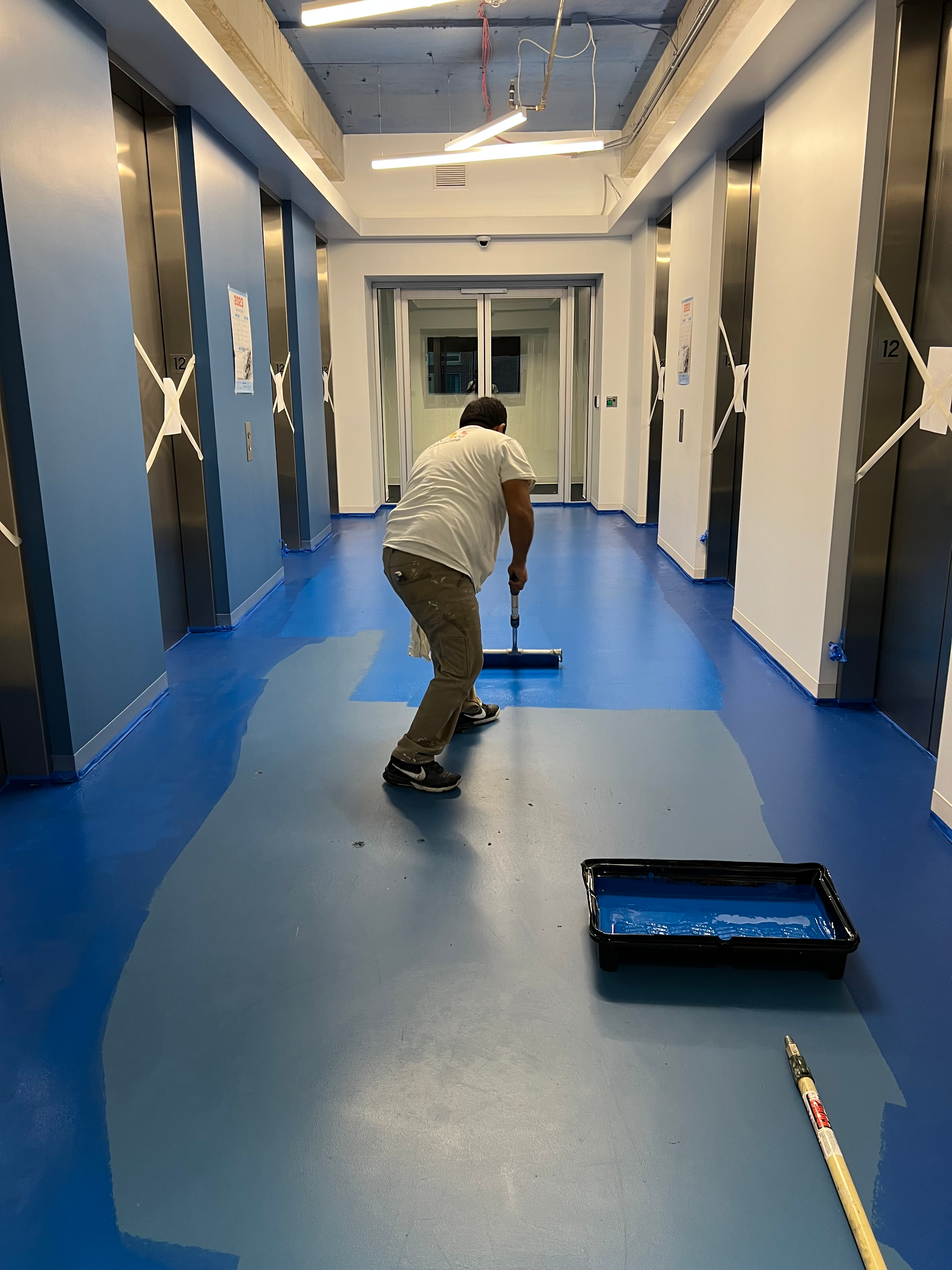 A man is painting a blue floor in a hallway
