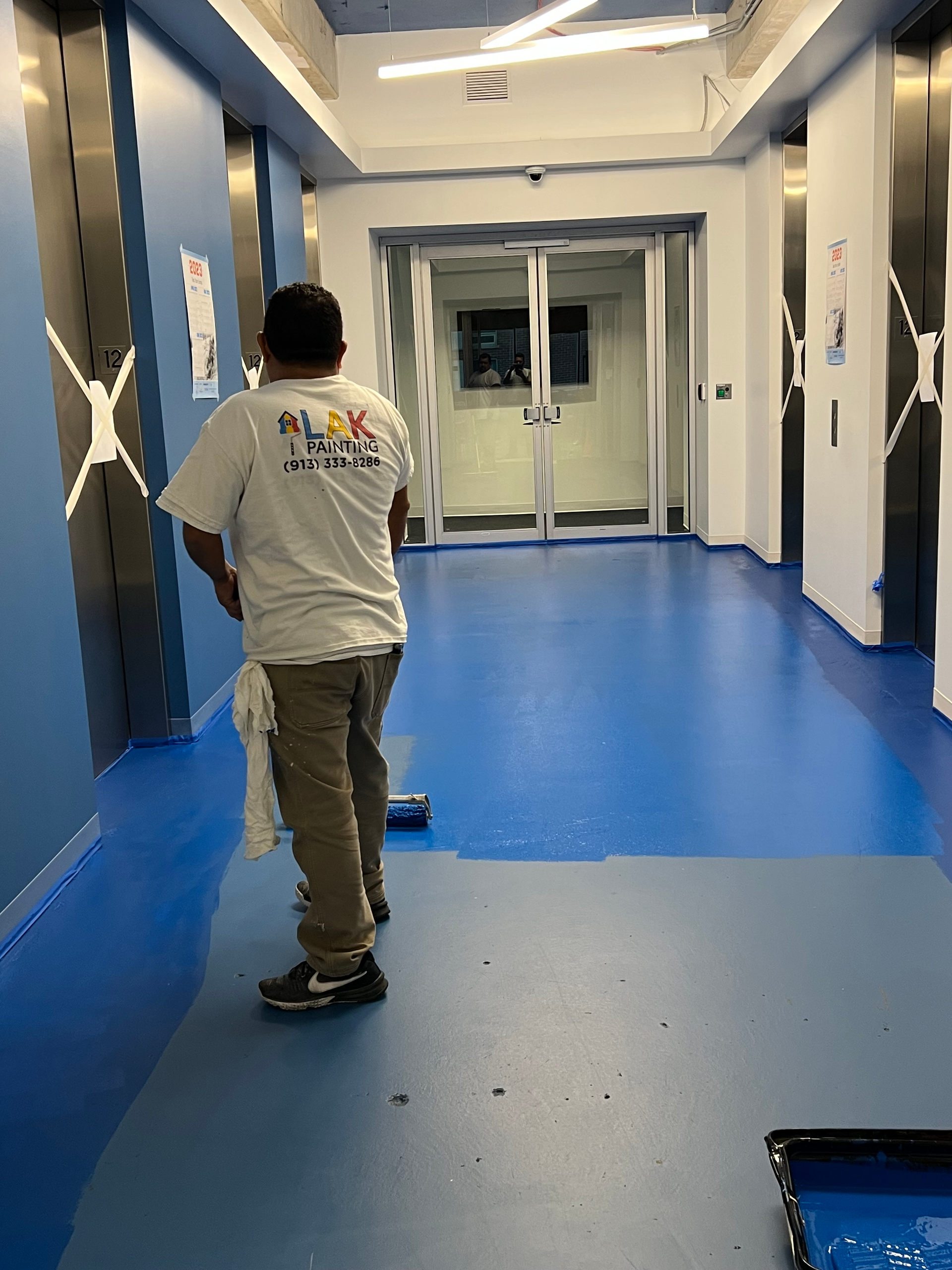 A man is painting a blue floor in a hallway