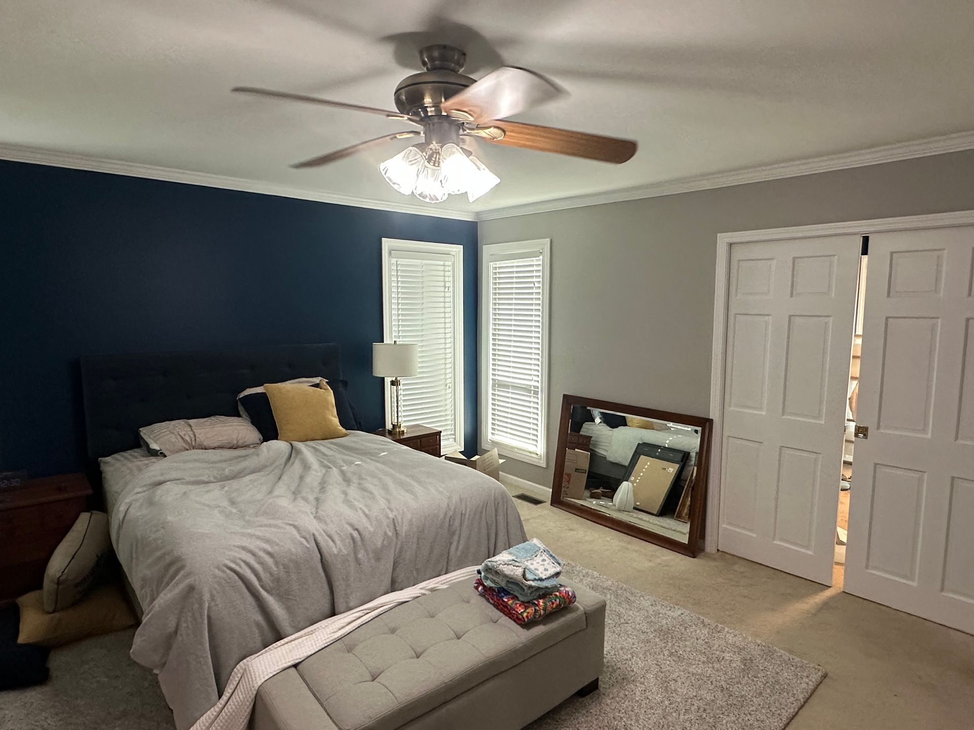 A bedroom with a bed , ceiling fan , mirror and ottoman.
